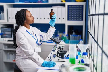 Afro-Amerikan kadın bilim adamı üniforması giyiyor. Panoya yazıyor. Şişe laboratuarına bakıyor.