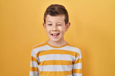 Sarı arka plan üzerinde duran genç beyaz çocuk kameraya seksi bir ifadeyle bakıyor, neşeli ve mutlu bir yüzle.. 