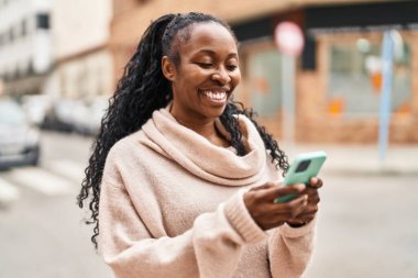Afro-Amerikalı kadın sokakta akıllı telefon kullanarak kendine güveniyor.