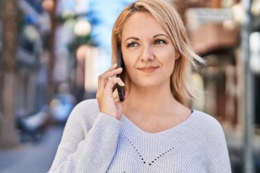 Genç sarışın kadın gülümsüyor. Kendine güveni tam. Akıllı telefondan konuşuyor.