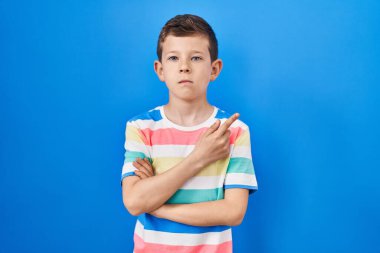 Mavi arka planda duran genç beyaz çocuk, elini yana uzatmış, ciddi ve sakin bir yüz ifadesi sergiliyor. 