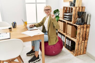 Ofiste çalışan güzel beyaz iş kadını bir fikir ya da soru işareti ile şaşırmış bir şekilde pilates topunda oturuyor. 