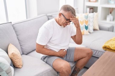 Orta yaşlı, kır saçlı, başı ve karnı ağrıyan bir adam.