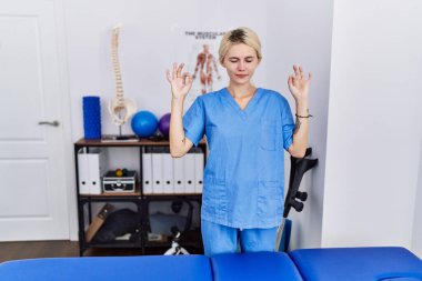 Ağrı kesici kliniğinde çalışan genç fizyoterapist kadın rahatlamış ve parmaklarıyla meditasyon hareketi yaparken gözleri kapalı gülümsüyor. yoga konsepti. 