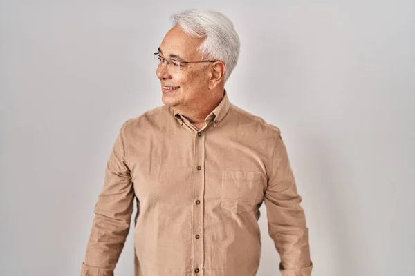 Hispanic senior man wearing glasses looking away to side with smile on face, natural expression. laughing confident.