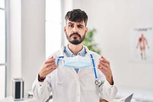Young Hispanic Doctor Man Beard Holding Safety Mask Skeptic Nervous — kuvapankkivalokuva