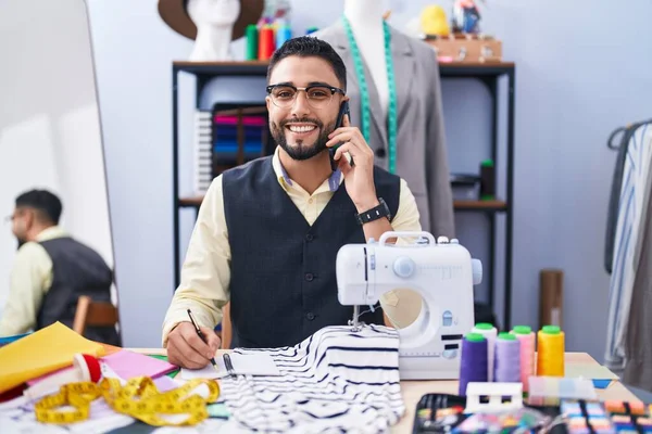 在服装厂 年轻的Arab男子裁缝在笔记本上谈论智能手机写作 — 图库照片