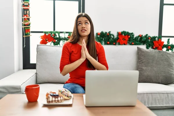 Молодая Брюнетка Ноутбуком Сидящая Диване Рождество Умоляя Молясь Руками Вместе — стоковое фото