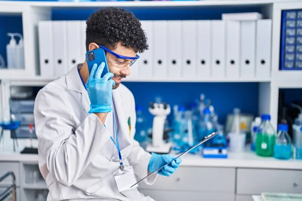 研究室のスマートフォンで科学者の制服を着た若いアラブ人男性 — ストック写真