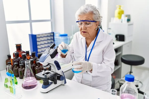 研究室で科学者の制服を着たシニア白髪の女性が液体を注ぐ — ストック写真