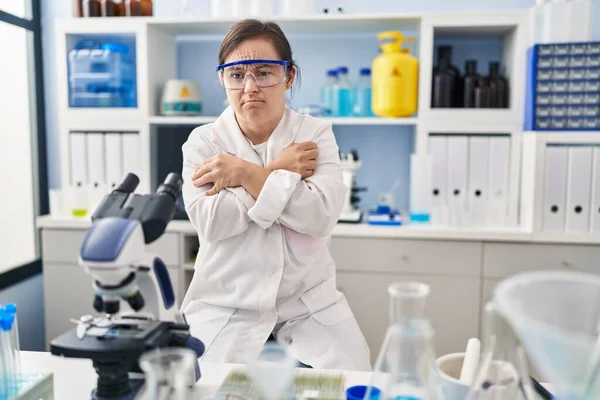 Hispanic girl with down syndrome working at scientist laboratory shaking and freezing for winter cold with sad and shock expression on face