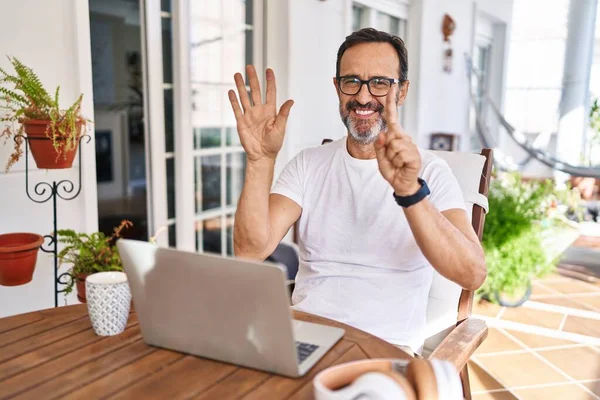 Middle age man using computer laptop at home showing and pointing up with fingers number six while smiling confident and happy.