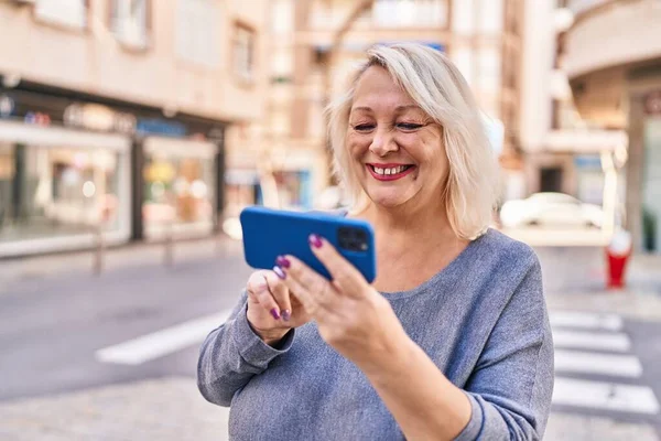 中世ブロンド女性スマートフォンを使用して自信を持って笑顔でストリート — ストック写真