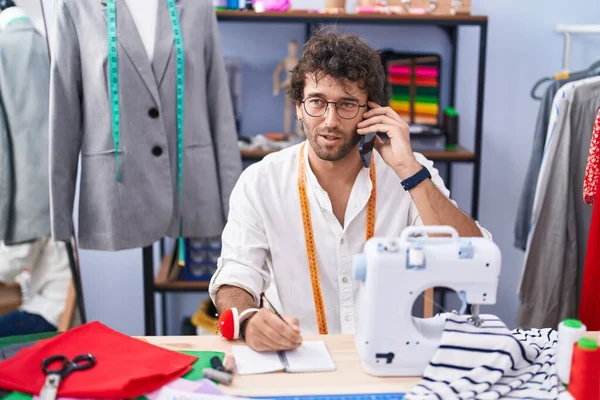 Joven Sastre Hispano Hablando Smartphone Escribiendo Cuaderno Fábrica Ropa — Foto de Stock