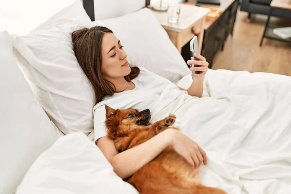 Νεαρή Ισπανίδα Που Αγκαλιάζει Σκύλο Και Χρησιμοποιεί Smartphone Ξαπλωμένη Στο — Φωτογραφία Αρχείου