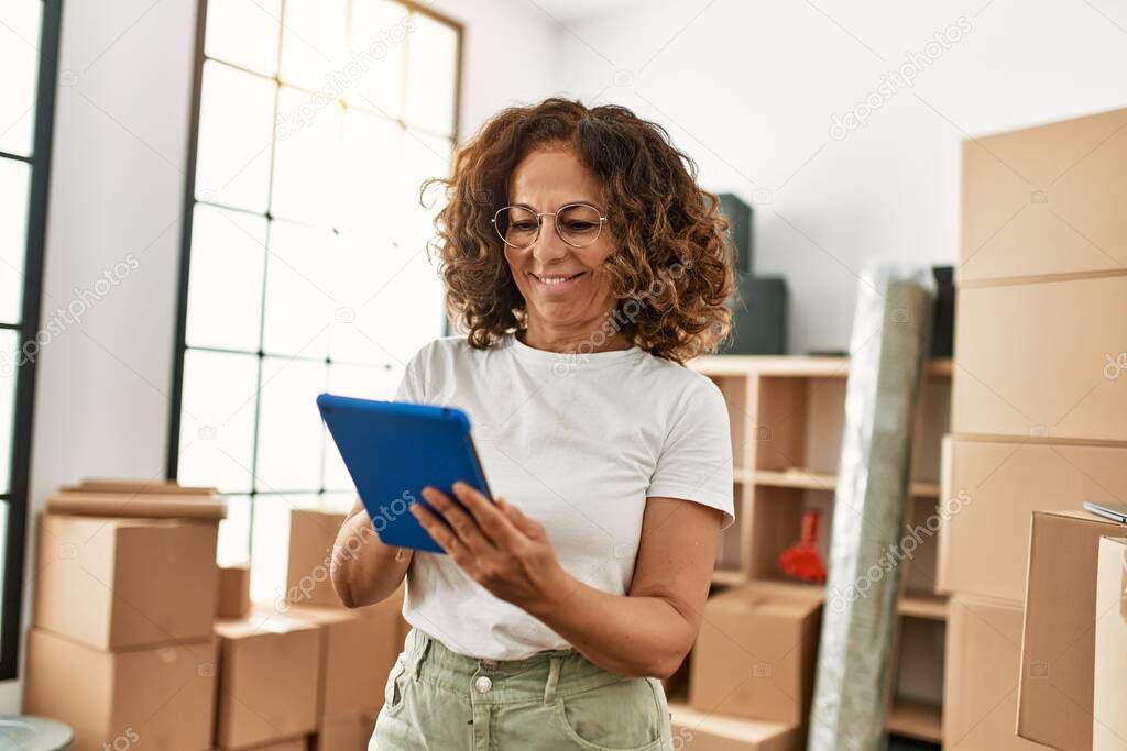 Middle age hispanic woman smiling confident using touchpad at new home