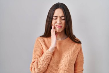Beyaz arka planda duran esmer bir kadın diş ağrısı ya da diş ağrısı yüzünden elleriyle dudaklarına dokunuyor. dişçi 