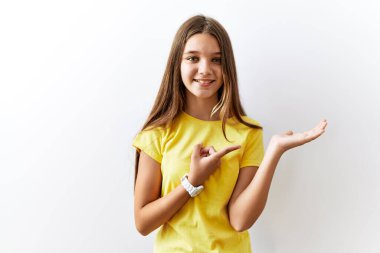 Young brunette teenager standing together over isolated background amazed and smiling to the camera while presenting with hand and pointing with finger. 