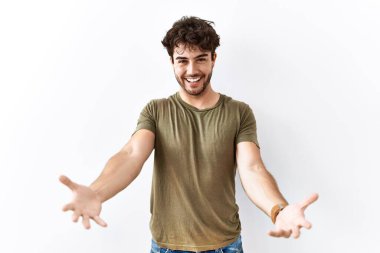 Hispanic man standing over isolated white background smiling cheerful offering hands giving assistance and acceptance. 