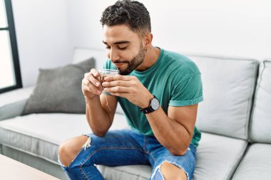 Genç Arap adam evdeki kanepede çay içiyor.