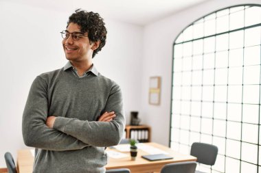 Genç İspanyol işadamı gülümsüyor. Kollarını kavuşturup ofiste mutlu duruyor..