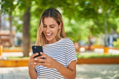 Parkta akıllı telefon kullanan, kendine güvenen genç sarışın kadın.