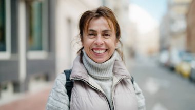 Orta yaşlı İspanyol kadın sokakta kendine güvenerek gülümsüyor.