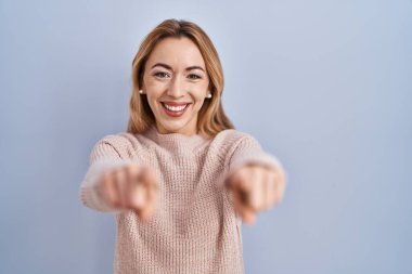 Mavi arka planda duran İspanyol kadın sana ve kameraya parmaklarıyla bakıyor, gülümsüyor pozitif ve neşeli. 