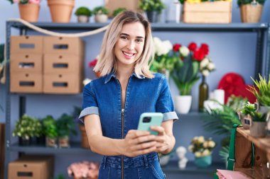 Young woman florist smiling confident using smartphone at florist