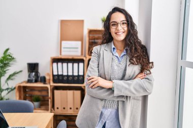 Genç İspanyol iş kadını gülümseyen kendine güvenen kollarını kavuşturup ofiste el kol kola duran.