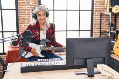 Middle age grey-haired woman musician playing electrical guitar at music studio