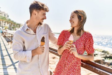 Genç İspanyol çift tatilde gülümseyerek kumsalda dondurma yiyor.