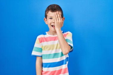 Mavi arka planda duran genç beyaz çocuk bir gözünü eliyle kapatıyor, yüzünde kendine güvenen bir gülümseme ve sürpriz bir duygu var.. 