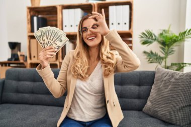 Terapi ofisinde çalışan genç sarışın kadın elinde para tutarken mutlu mesut gülümsüyor. 