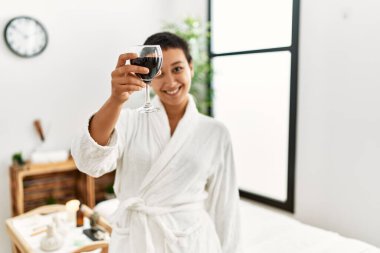 Genç İspanyol kadın bornoz giyip güzellik merkezinde şarap içiyor.