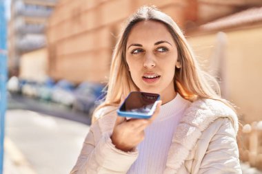 Gülümseyen genç bir kadın caddedeki akıllı telefondan konuşuyor.