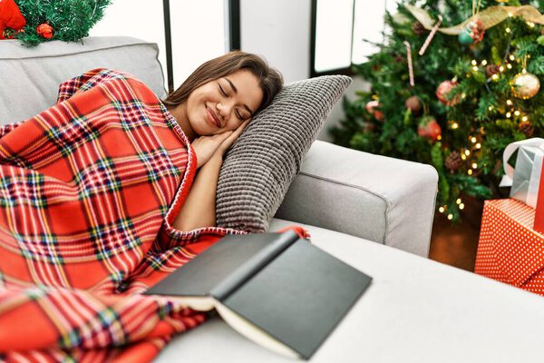 Молодая латинская женщина спит на диване у рождественской елки дома
