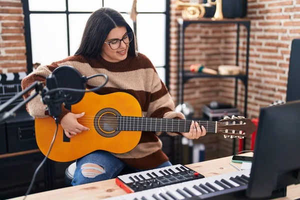 Young hispanic woman musician playing spanish guitar at music studio