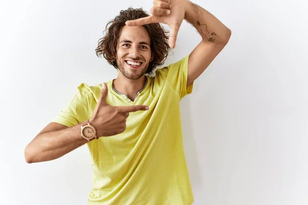 幸せな顔で手や指でフレームを作る孤立した背景笑顔の上に立っている若いヒスパニック系の男 創造性と写真の概念 — ストック写真
