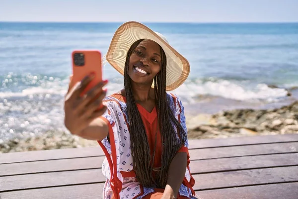 Genç Afrikalı Amerikalı turist sahildeki bankta oturan akıllı telefonun yanında selfie çekiyor..