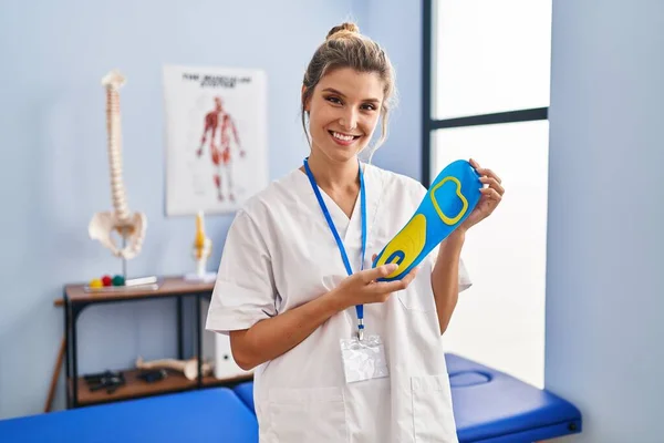 Young woman holding shoe insole at physiotherapy clinic smiling with a happy and cool smile on face. showing teeth.