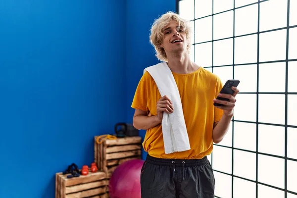 Young blond man smiling confident using smartphone at sport center