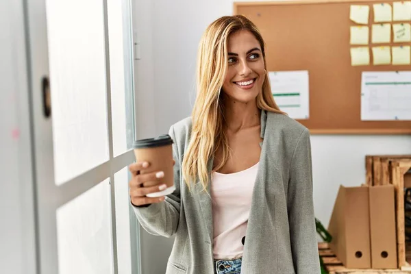 若い白人実業家がオフィスの窓のそばに立ってコーヒーを飲む — ストック写真