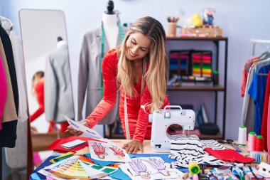 Terzi dükkanında kendine güvenen, sırıtan genç sarışın kadın.