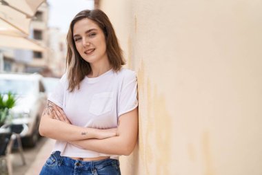 Kendine güvenen genç bir kadın caddede kollarını kavuşturmuş duruyor.