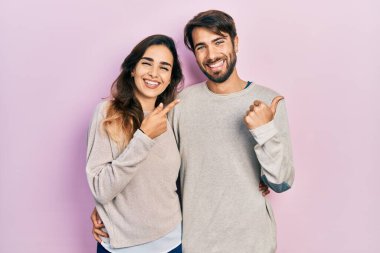 Gündelik giysiler giymiş genç İspanyol bir çift elleri ve başparmakları havada, kendinden emin bir şekilde arka tarafı işaret ediyor. 