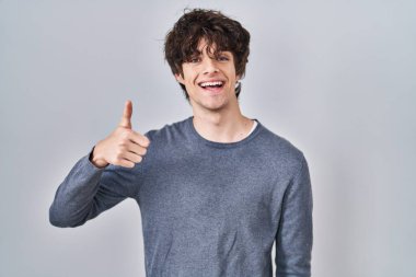 İzole edilmiş arka planda duran genç adam elleriyle mutlu bir jest yapıyor. Kameraya bakıp başarıyı gösteren ifade. 