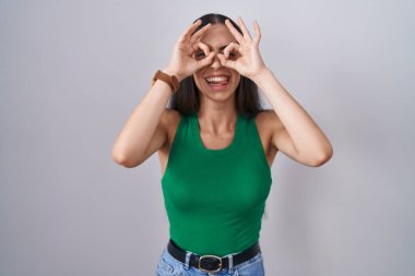 Tecrit edilmiş arka planda duran genç bir kadın dürbün gibi jest yapıyor, dili dışarı çıkarıyor, gözler parmaklarından bakıyor. çılgın ifade. 