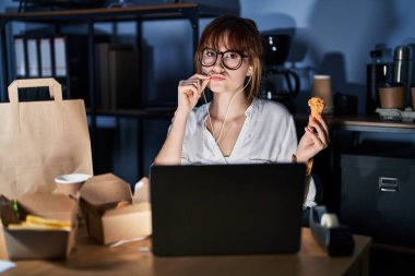 Genç ve güzel bir kadın bilgisayarla çalışıyor ve yemek dağıtıyor ağızları ve dudakları parmaklarıyla kapalı. gizli ve sessiz, tabu konuşması 