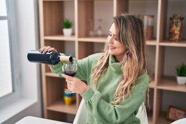 Young woman smiling confident pouring wine on glass at home